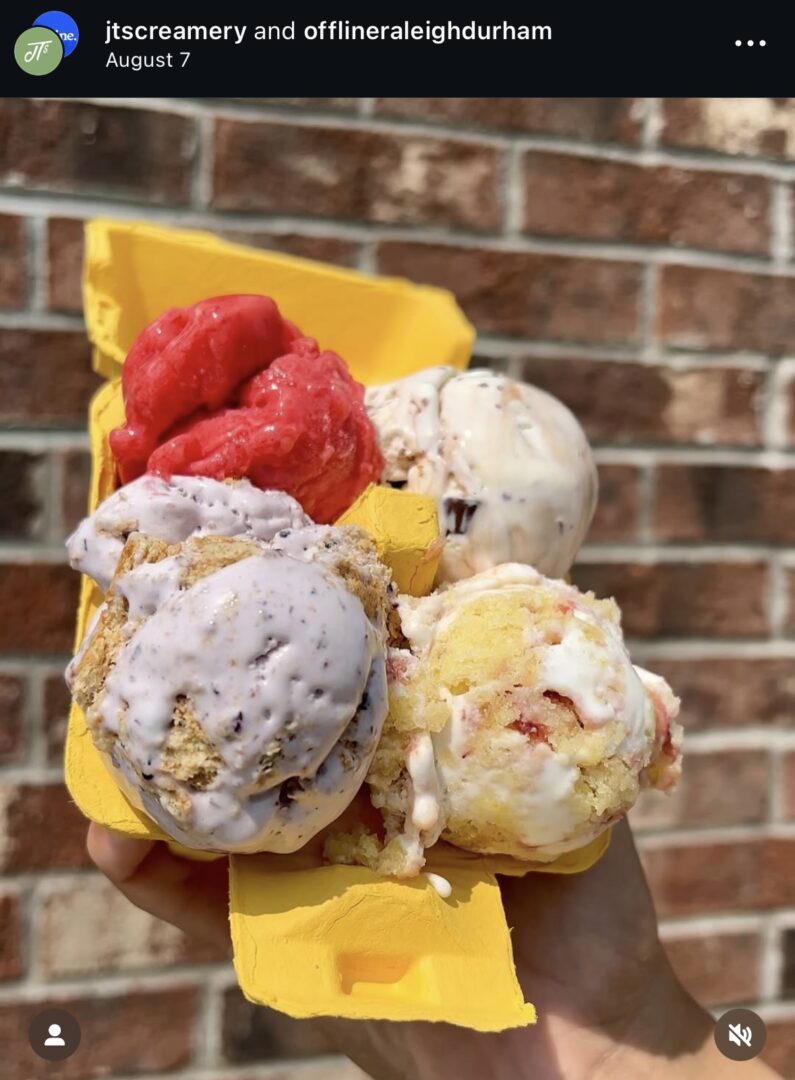Hand holding colorful ice cream scoops outdoors.