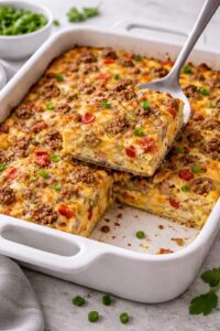 Breakfast casserole with eggs, sausage, cheese, and vegetables baked in a dish with a slice removed