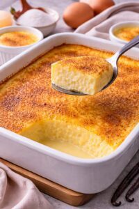 Classic baked custard with nutmeg in a baking dish with a spoon lifting a creamy portion